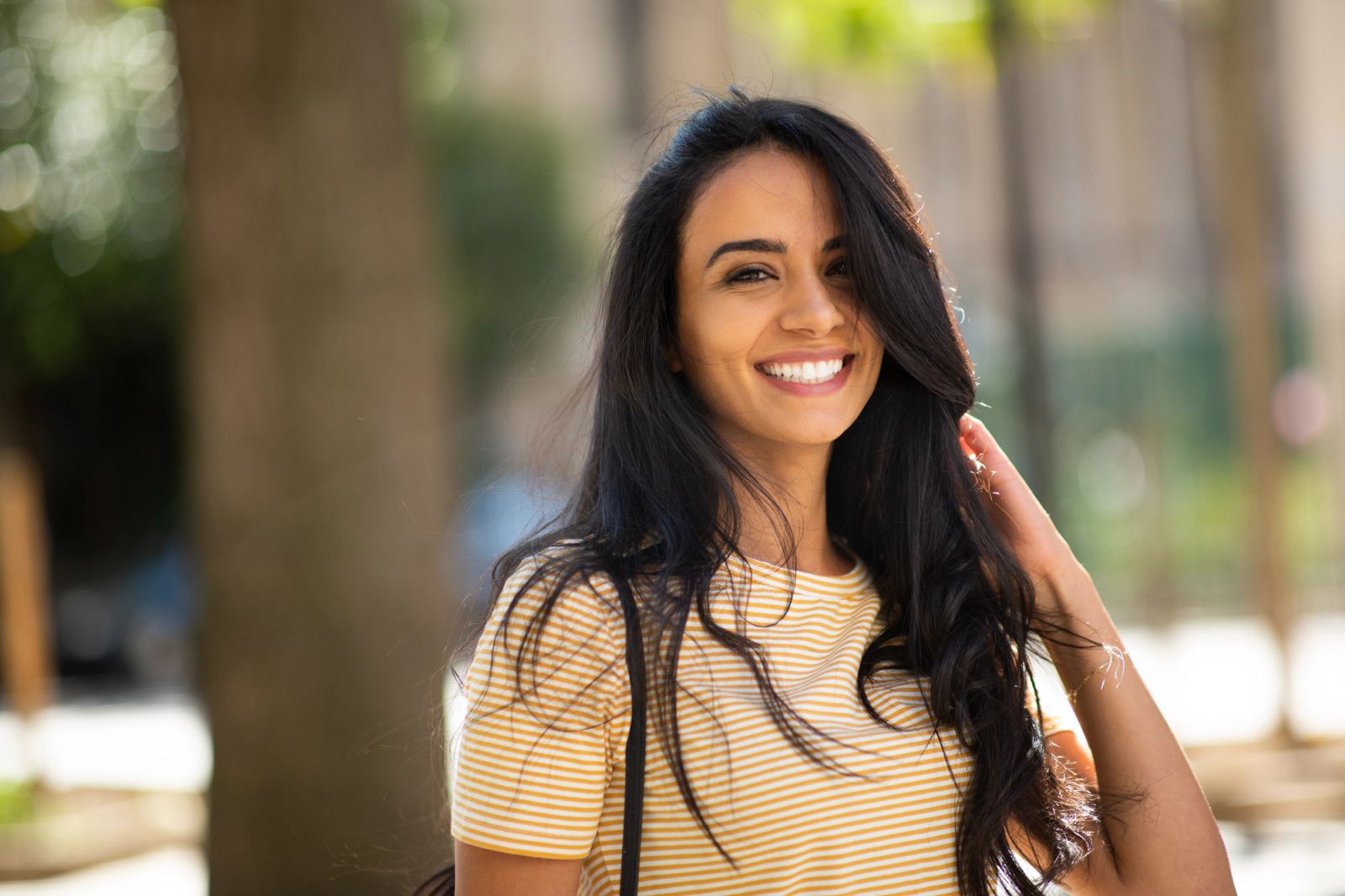 Smiling woman with long dark hair in a striped shirt outdoors.
